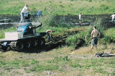 1992 Ford Bronco - People work around a tracked vehicle in a muddy field, with more individuals visible in the background.