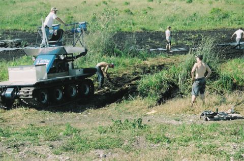 1992 Ford Bronco - People work around a tracked vehicle in a muddy outdoor area.