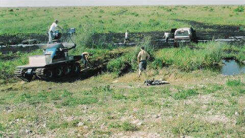 1992 Ford Bronco - People attempt to free vehicles stuck in a muddy, grassy area.