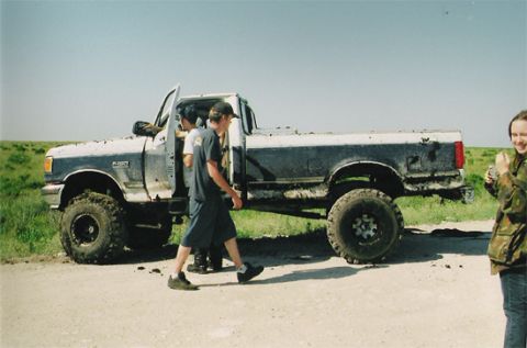1992 Ford Bronco - A lifted pickup truck, heavily mud-splattered, is seen from the side with people entering and exiting.