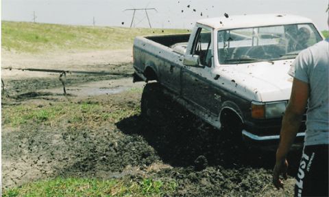 1992 Ford Bronco - A white Ford pickup truck is stuck in thick mud, with mud splattering around it.