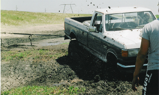 White Ford pickup truck stuck in mud, mud flying
