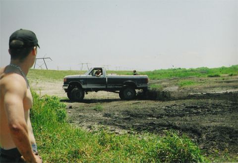 1992 Ford Bronco - A lifted Ford F-Series truck navigates a muddy terrain, kicking up dirt as it goes.