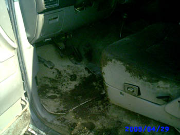 1992 Ford Bronco - Interior shot through an open door showing a passenger footwell and gray cloth seat caked in dried mud, with mud smeared across the carpet,…