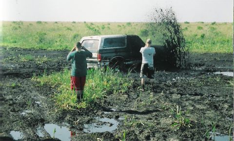 1992 Ford Bronco - Scanned photo of a full-size SUV with a white top buried in a mud pit, throwing a large rooster tail of mud into the air from a spinning ti…