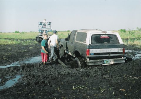 1992 Ford Bronco - A 1992 Ford Bronco is stuck deep in the mud, with two people nearby and a tracked vehicle in the background.