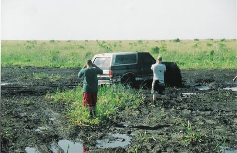 1992 Ford Bronco - A 1992 Ford Bronco is stuck in a muddy field with two people observing the situation.