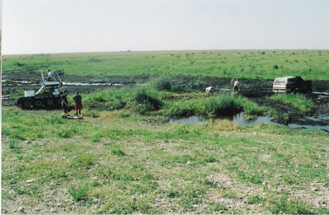 1992 Ford Bronco - A dark SUV is stuck in the mud next to a tracked vehicle with people around.