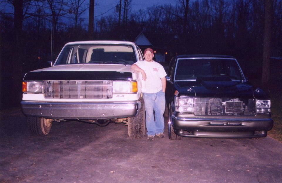 Man standing between a white 1987 Ford F-150 and a dark 1980s Chevrolet pickup