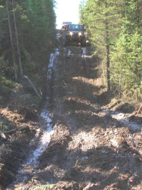 2003 Jeep TJ - Two Jeeps navigate a challenging muddy incline in a wooded area.