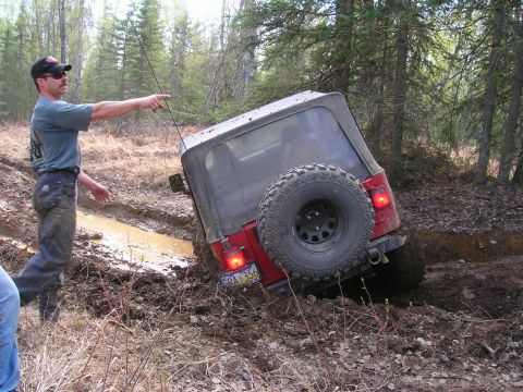 2003 Jeep TJ - A man directs attention to a red Jeep Wrangler that has become stuck in a muddy trail during an off-road excursion.