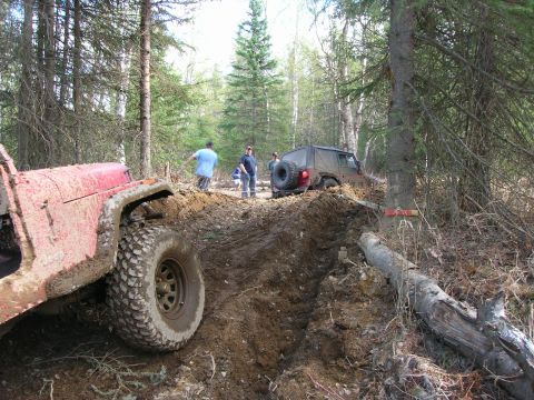 2003 Jeep TJ - Two Jeep TJs navigate a challenging muddy off-road course in a wooded area.