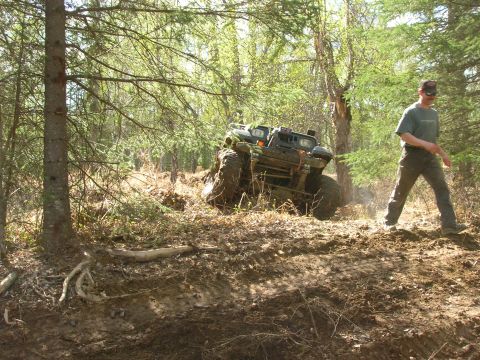 2003 Jeep TJ - An all-terrain vehicle navigates a challenging, muddy trail in a wooded area.