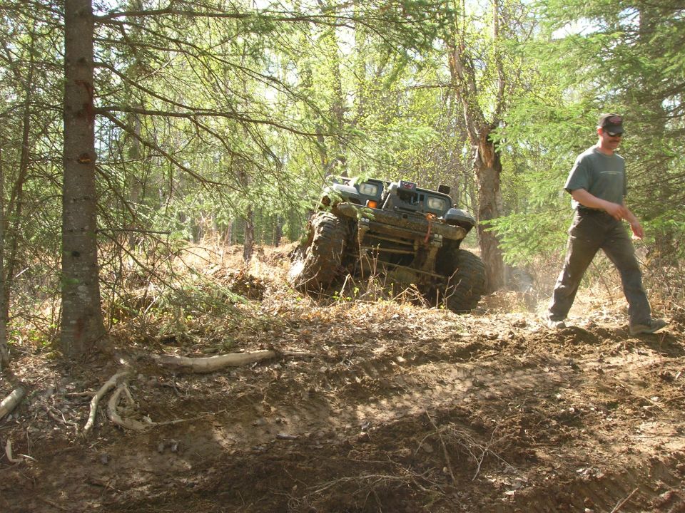 ATV going through muddy woods with a person walking nearby