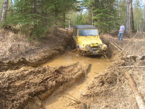 2003 Jeep TJ - A yellow 2003 Jeep TJ navigates a muddy trail, kicking up water and dirt.