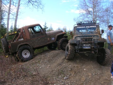 2003 Jeep TJ - Two modified Jeeps navigate a challenging off-road trail under a partly cloudy sky.