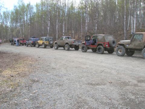 2003 Jeep TJ - A convoy of off-road vehicles, including several Jeeps and a pickup truck, are parked on a gravel road.