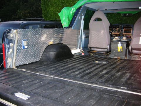 1985 Ford Bronco - The interior of a pickup truck bed shows diamond plate lining and custom bucket seats.