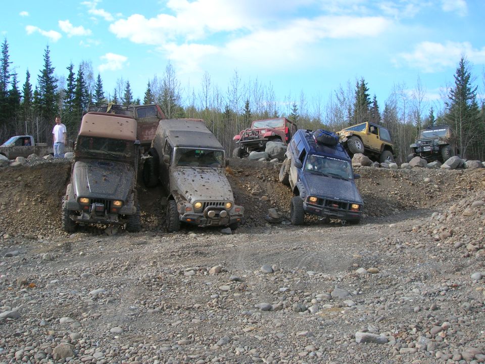 Several off-road vehicles navigating a rocky incline under a partly cloudy sky