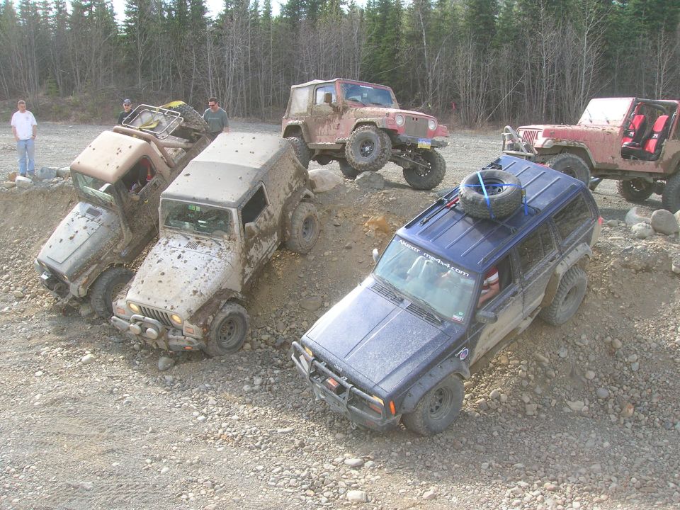 Several Jeeps are driving on a dirt and rock trail. One blue Jeep Cherokee is in the foreground