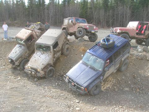 2003 Jeep TJ - Several Jeeps are navigating a challenging off-road course with muddy conditions.