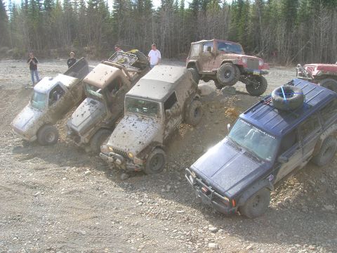 2003 Jeep TJ - A group of off-road vehicles are parked on a rocky, muddy hill, with trees in the background.