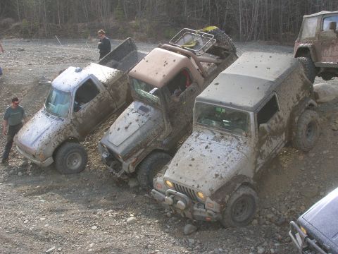 2003 Jeep TJ - Multiple off-road vehicles are covered in mud on a rocky terrain.