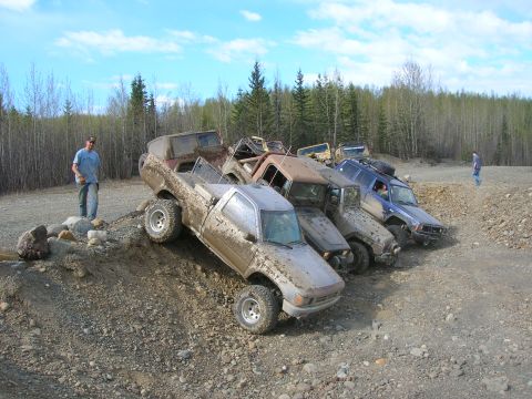 2003 Jeep TJ - Multiple off-road trucks are parked on a dirt hill, with a man observing the scene.