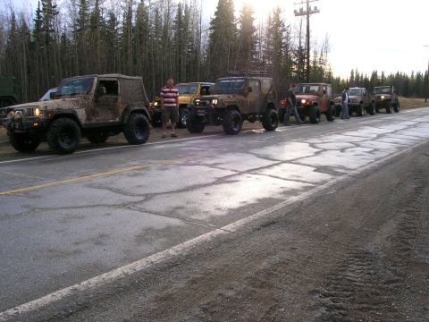 2003 Jeep TJ - Several muddy Jeeps are lined up on the side of a road, with people standing near them.