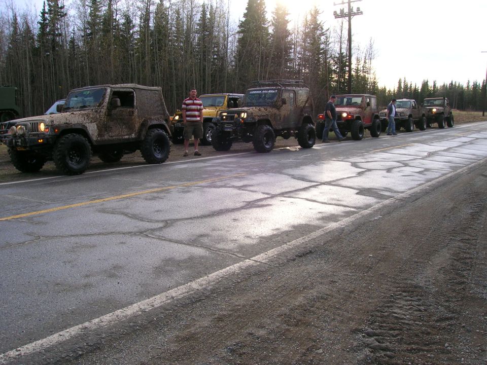 Line of muddy Jeeps parked on the side of a road with trees in the background. 2003 Jeep TJ is visible