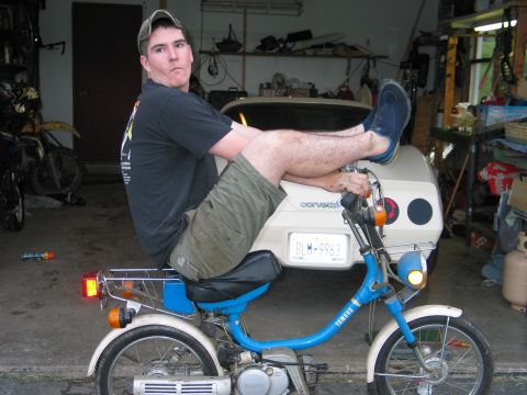 1993 Suzuki RMX250 - A man poses on a blue Yamaha moped in a cluttered garage.