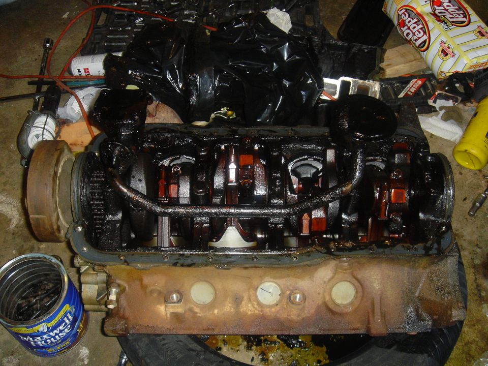 Engine block with crankshaft exposed, covered in oil. Maxwell House coffee can visible