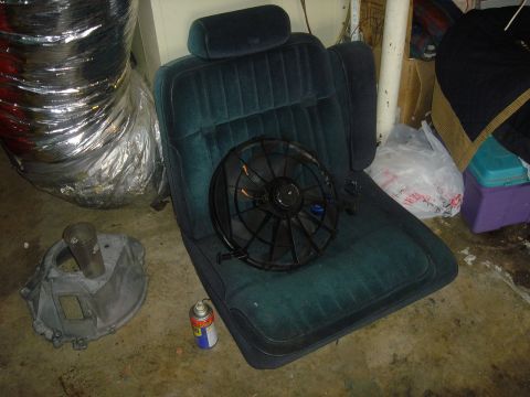 1986 Ford Mustang - A car seat is shown with a fan placed on it, alongside other automotive parts and supplies.