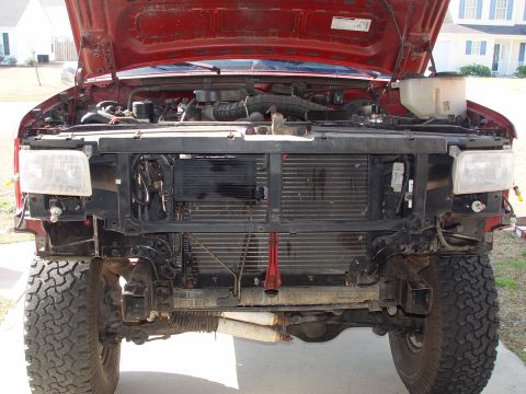 1994 Ford Bronco - The front end of a red 1994 Ford Bronco is disassembled with the hood open, revealing the engine and radiator assembly.