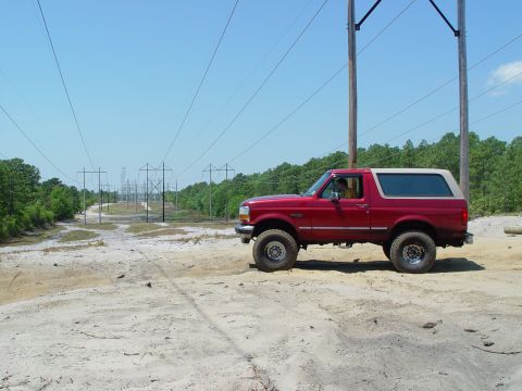1994 Ford Bronco - Red 1994 Ford Bronco parked on a sandy dirt path under a clear blue sky.