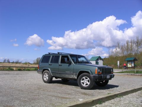 2000 Jeep Cherokee - A green Jeep Cherokee is parked in an outdoor lot under a partly cloudy sky.