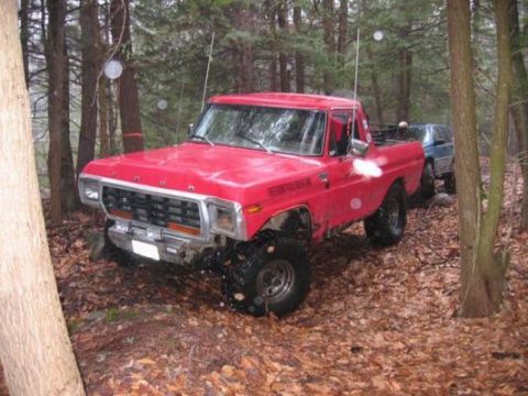 1978 Ford Bronco - A red pickup truck navigates a wooded terrain with another vehicle in the background.