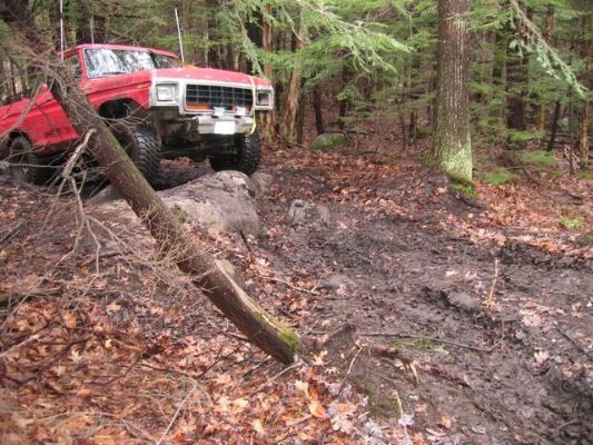 Red truck on a muddy, wooded trail, going over a log