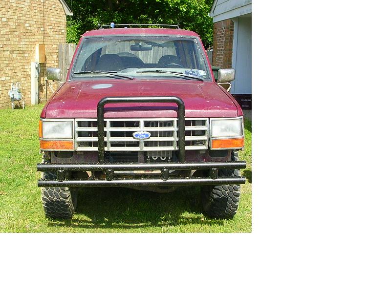Front view of lifted maroon Ford SUV with black tube bumper and grille guard on grass