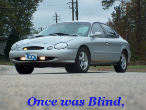 1998 Ford Taurus - This 1998 Ford Taurus is captured in a front 3/4 view, showing its silver exterior and a portion of the road it is traveling on.