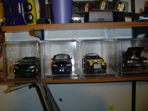1979 Ford Bronco - A collection of four model cars are displayed in individual clear cases on a wooden shelf.