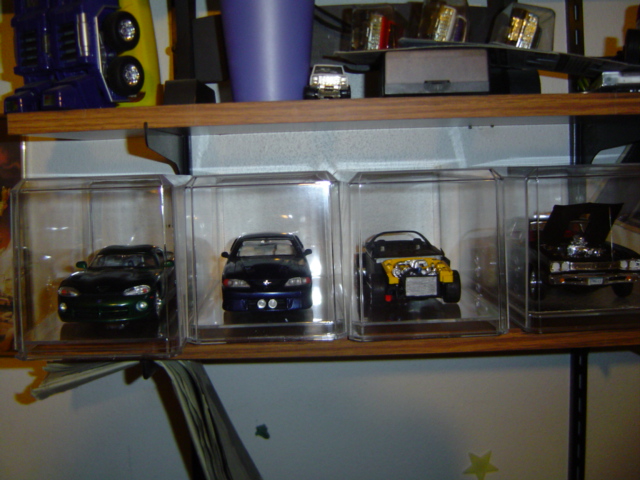 Four model cars displayed in clear cases on a shelf