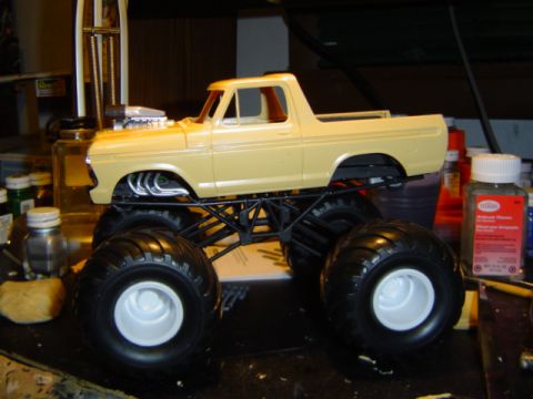 1979 Ford Bronco - A model of a monster truck sits on a workbench, surrounded by hobby supplies.