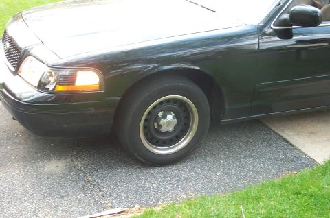 1999 Ford Crown Victoria - Close front three-quarter view of a dark green Ford Crown Victoria's driver side, showing the amber corner lamp, mesh grille and body-color…
