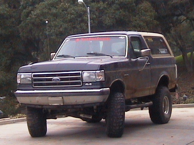 Dark blue Ford Bronco with a tan top, lifted suspension, and off-road tires, seen from a low front angle