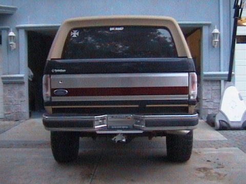 1991 Ford Bronco - This 1991 Ford Bronco is seen from the rear, a tan camper shell and a dark body with a chrome bumper.