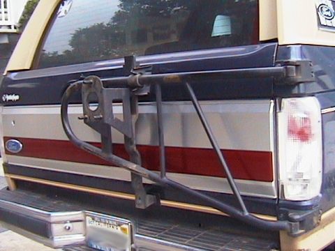 1991 Ford Bronco - Rear view of a dark blue and tan Ford Bronco tailgate with a bare black swing-out tire carrier mounted across it, the spare tire removed so…
