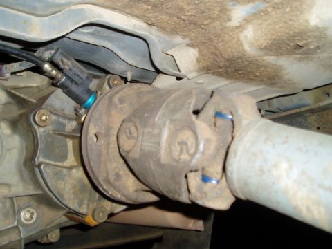 1990 Ford Bronco - Underside view of a transfer case and driveshaft slip yoke connection, with a rusty output flange marked with cast numbers and blue paint m…