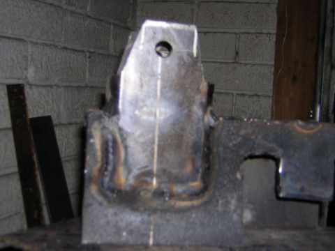 1995 Ford Bronco - A close-up of a custom-welded metal bracket, likely a vehicle part, against a brick wall.