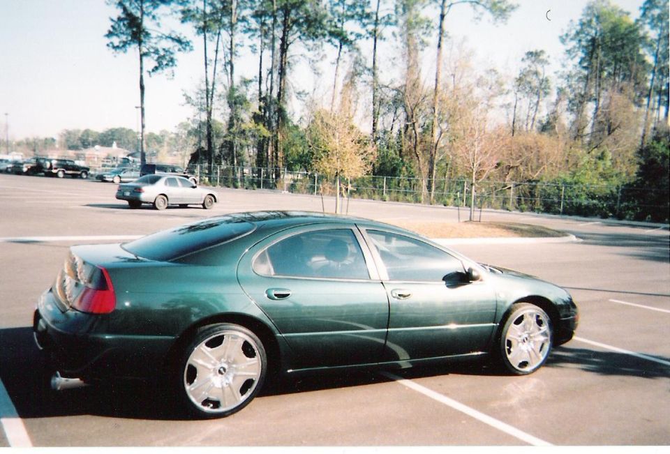 Dark green sedan in side profile parked in an empty lot with chrome wheels